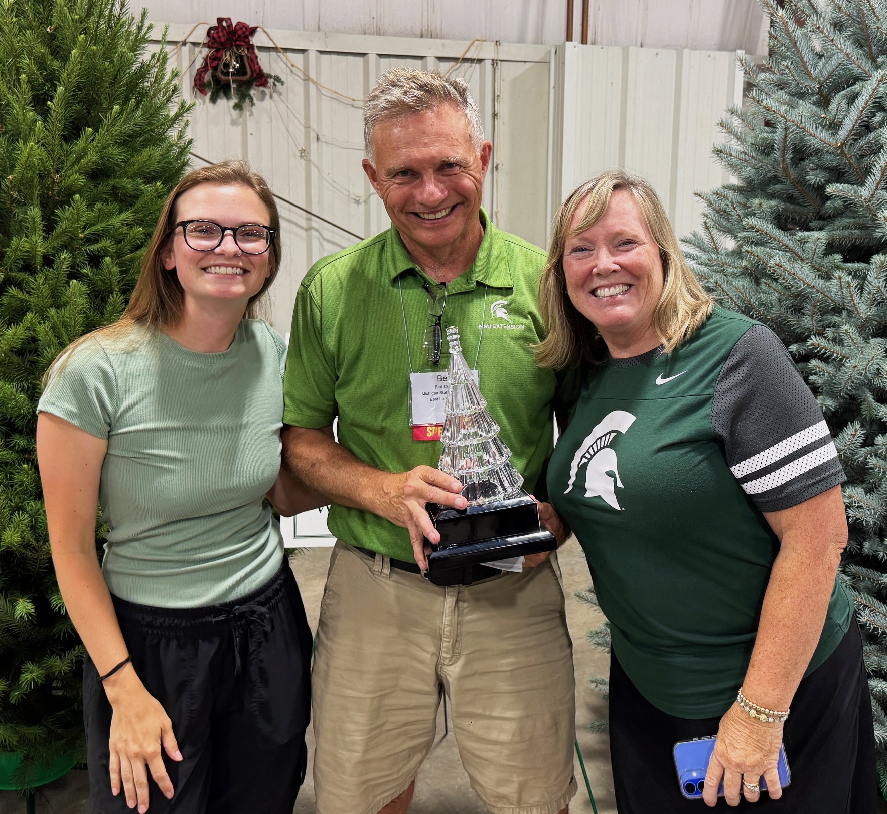 Riley, Bert and Terri pose with an award in front of Christmas trees.